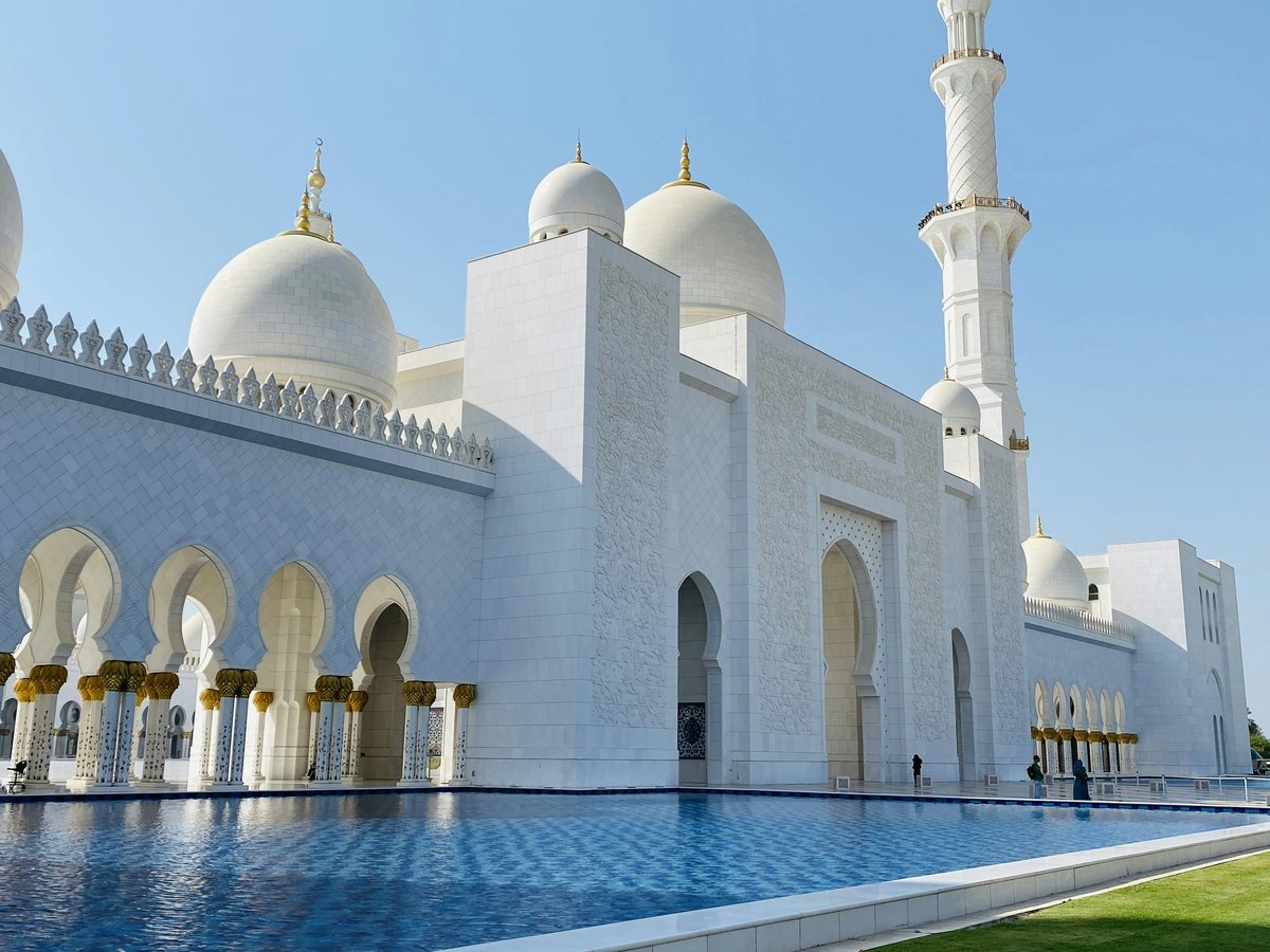 a large white building with domes and towers by a body of water with Sheikh Zayed Mosque in the background