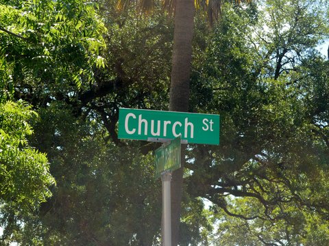 A green street sign reading Church St below a palm tree and leafy trees
