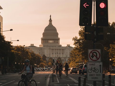 people biking on road and different vehicles viewing United States Capitol during daytime screenshot