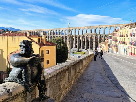 A statue overlooks the ancient roman aqueduct and city buildings.