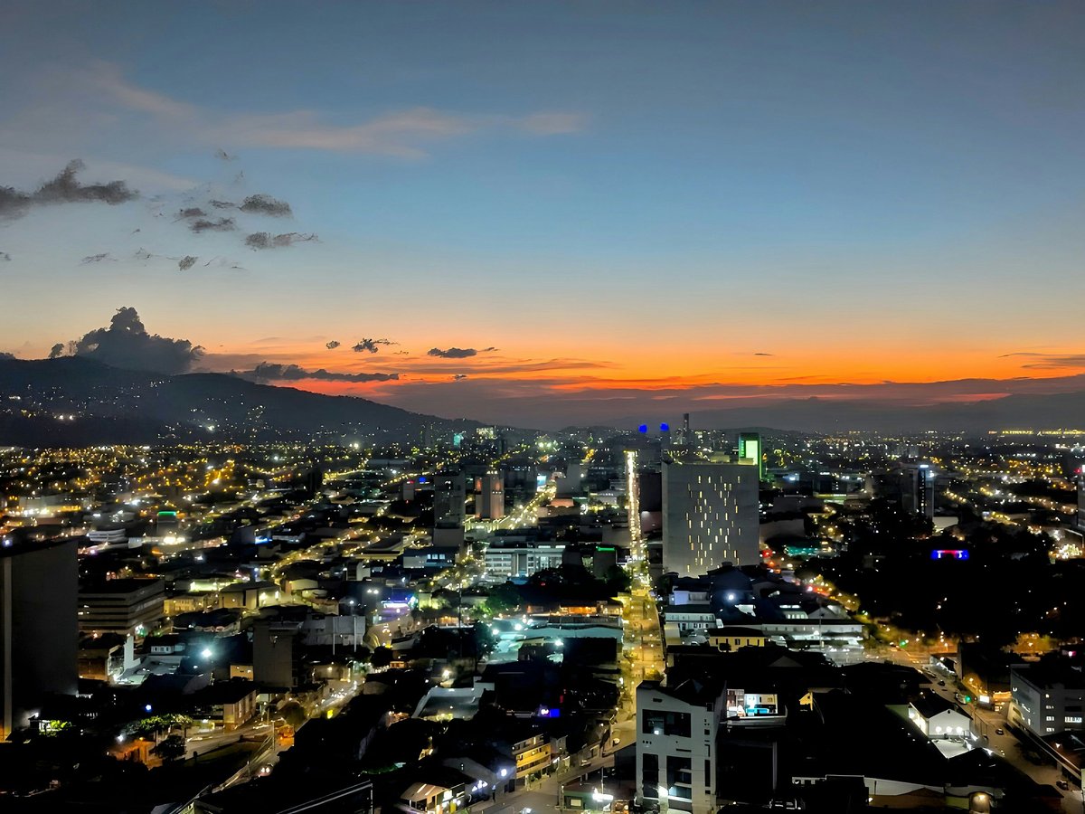 Nighttime cityscape shows lights and mountains.