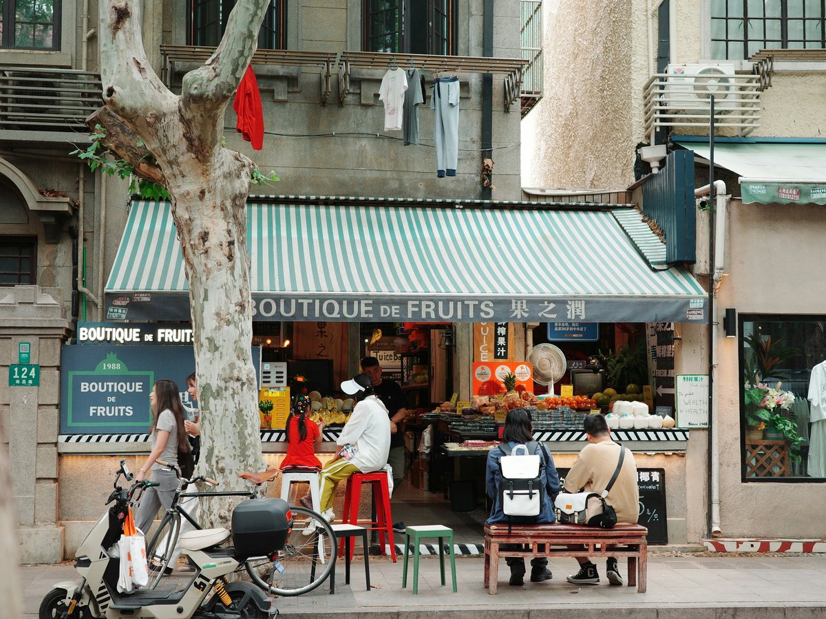 A fruit shop with people and a scooter.