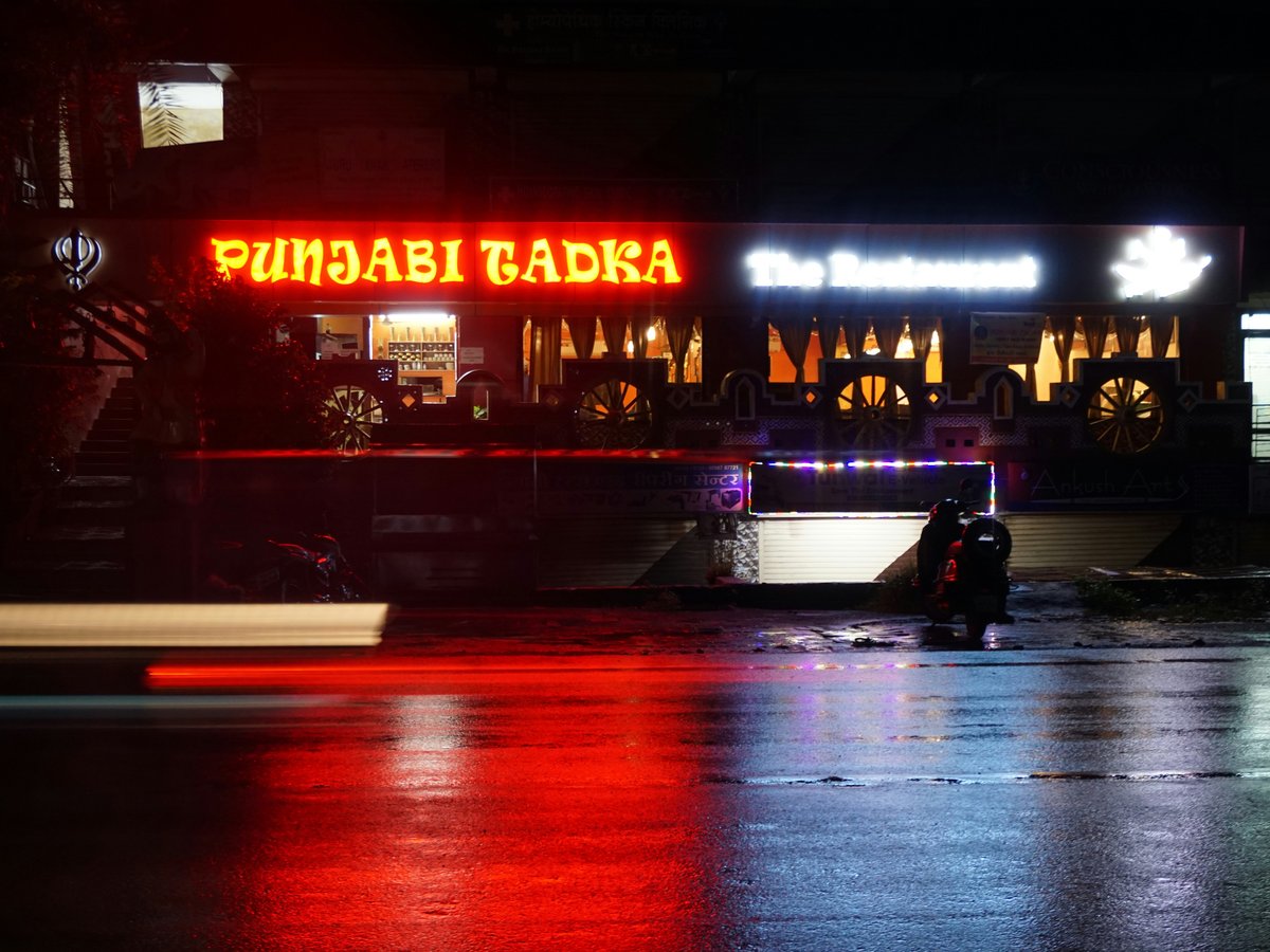 man in black jacket sitting on bench in front of store during night time