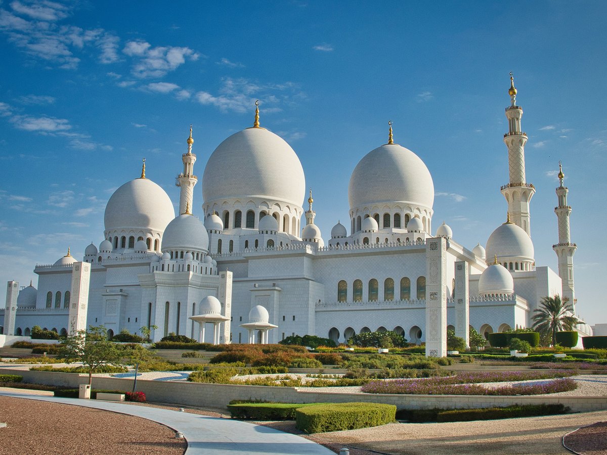 Grand white mosque with domes and minarets under blue sky.