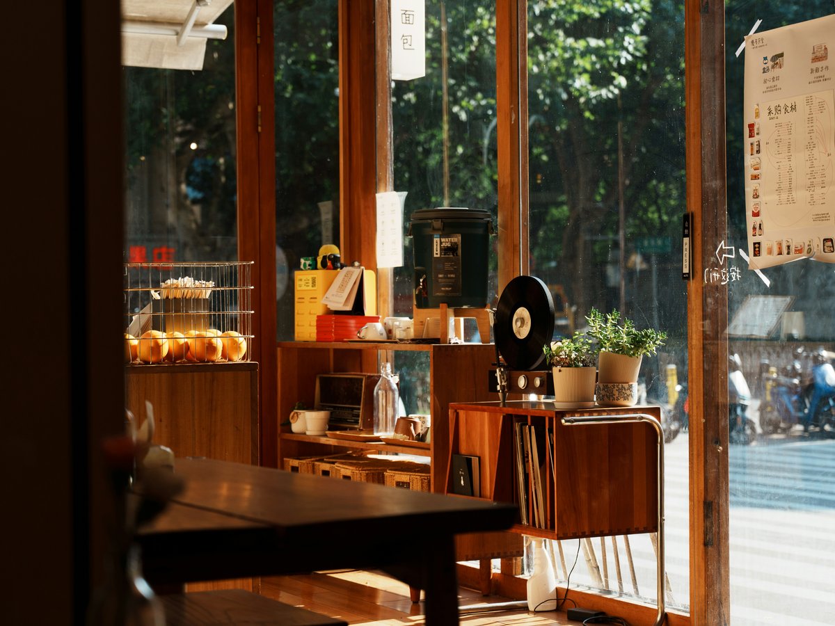 A sunlit cafe interior with wooden furniture, potted plants, and a vinyl record player