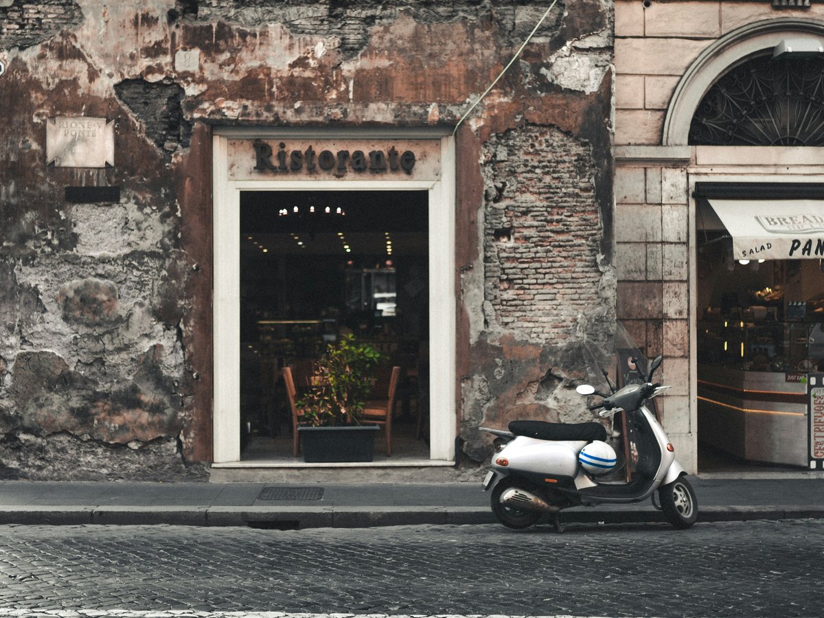black and white motor scooter parked beside brown concrete building during daytime