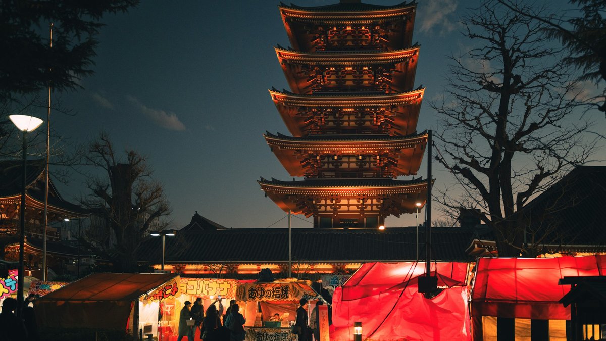 Senso-ji's five-story pagoda rises above a lantern-lit Nakamise-dori after dark, market stalls glowing saffron and gold as the wooden tiers stack into the violet Asakusa sky