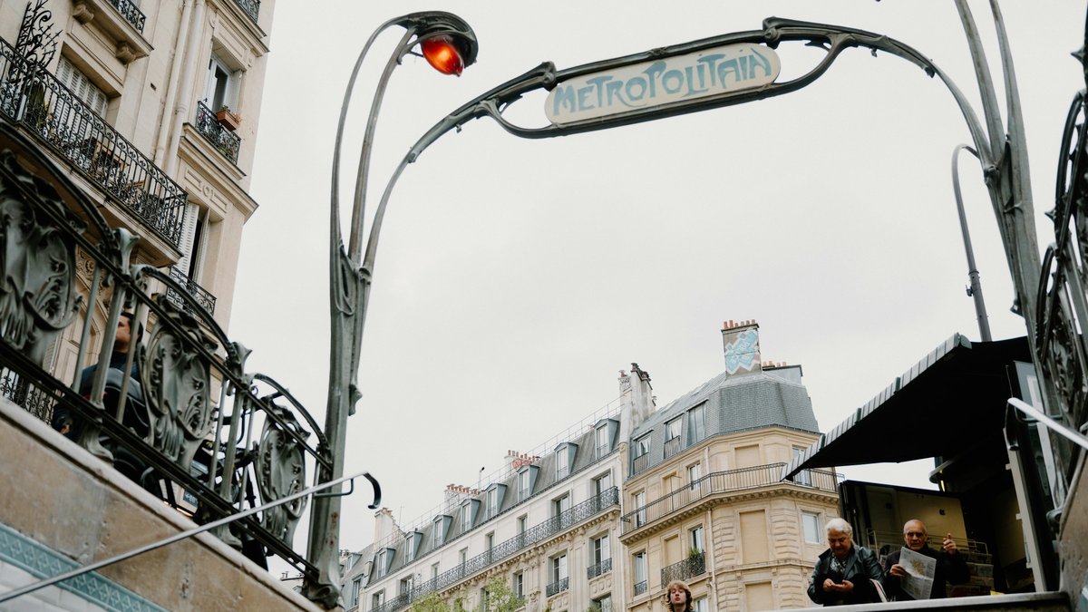 An Art Nouveau Métropolitain arch curving above a descending flight of metro stairs, Haussmann facades rising softly in the background