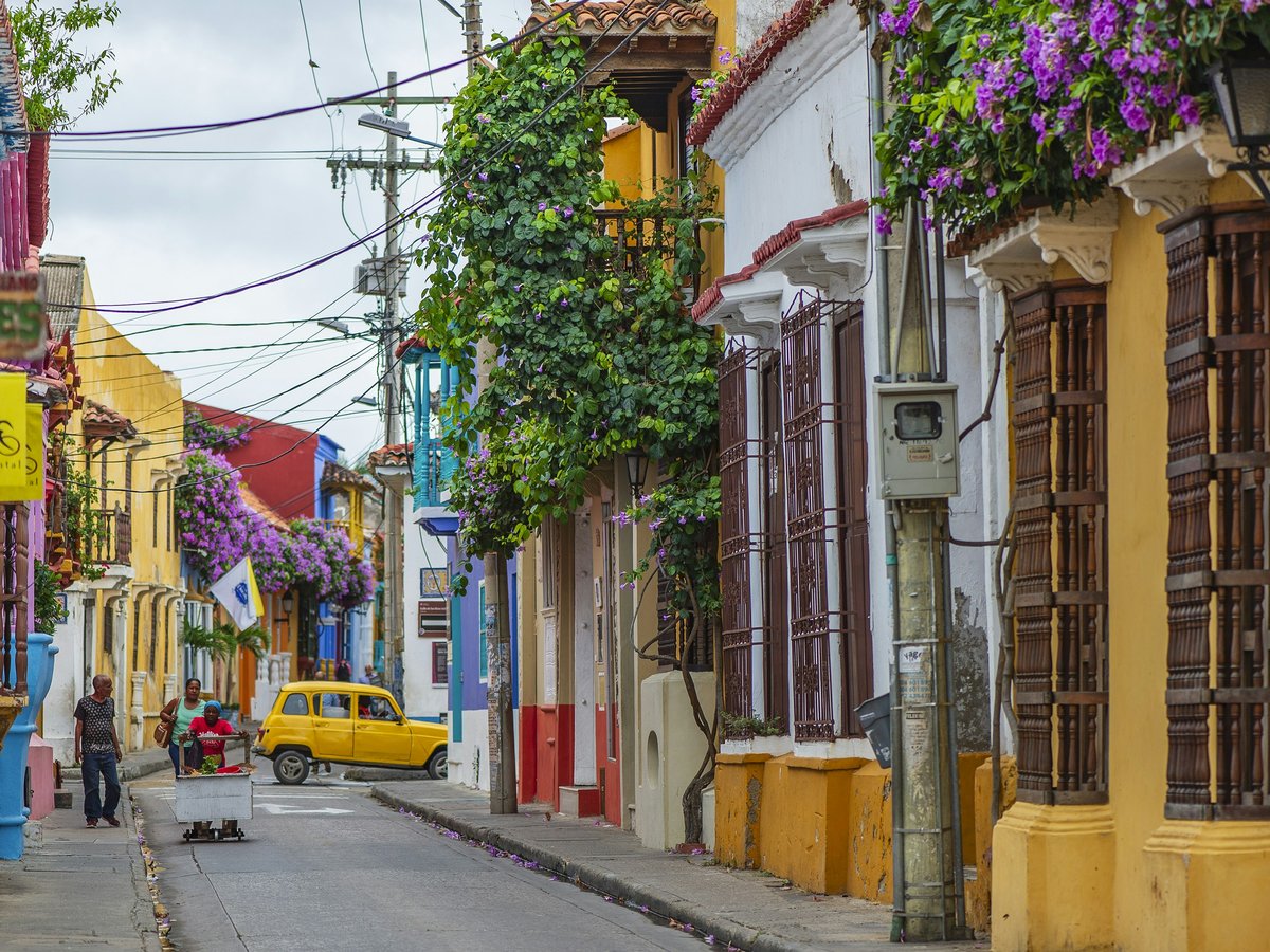 a yellow car driving down a street next to tall buildings