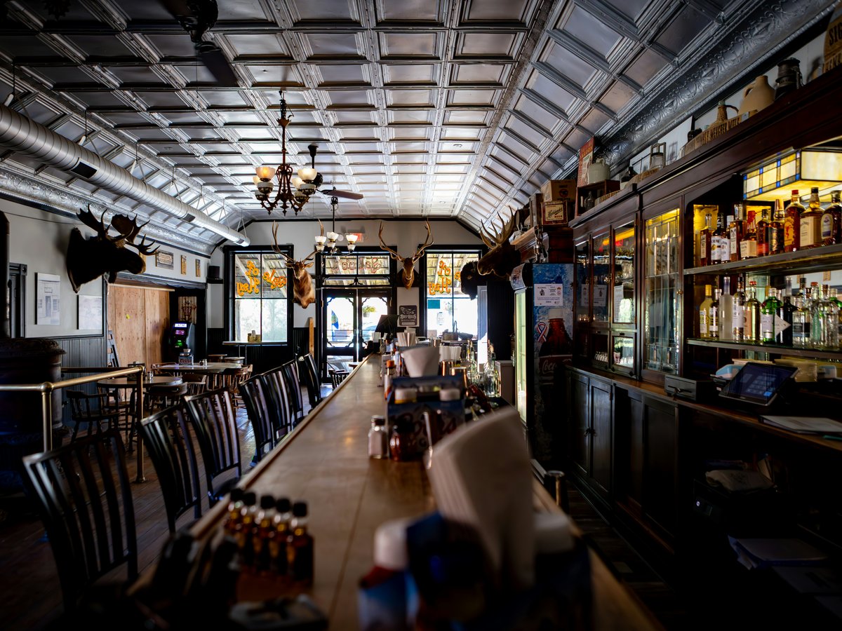 Empty bar interior with tables and bar shelves of bottles.