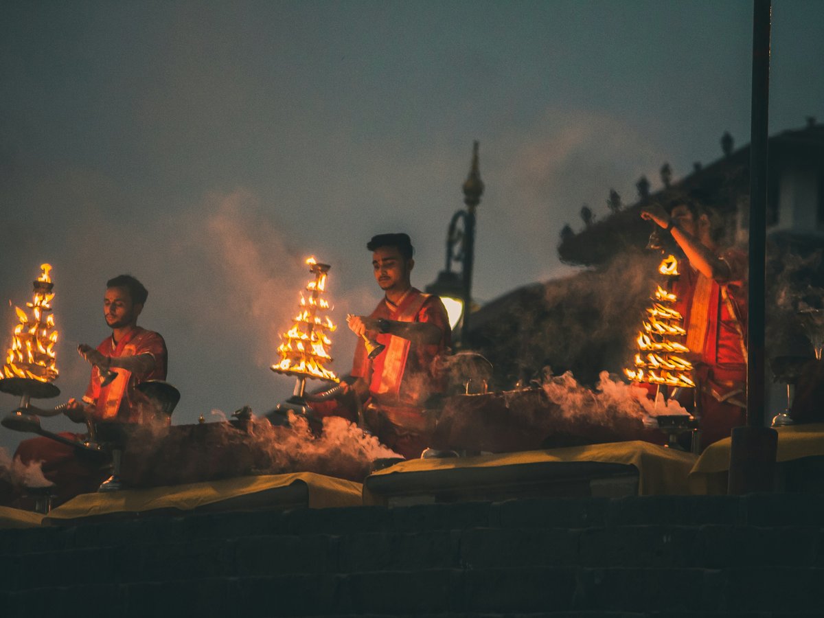 Three men in red robes performing a ritual with flaming tiered lamps at night