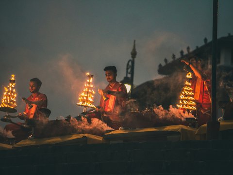Three men in red robes performing a ritual with flaming tiered lamps at night
