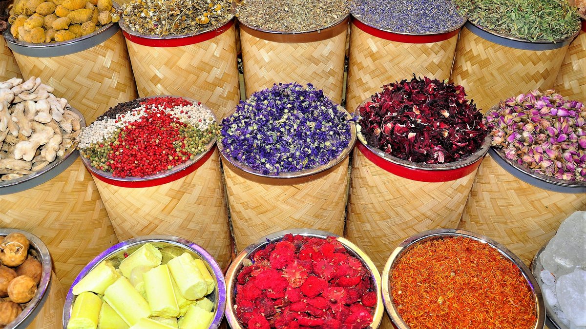 Deira Spice Souk baskets brimming with chamomile, dried roses, saffron, hibiscus, crushed chili, paprika and crystallised citrus, the rough woven rims stamped with red bands and staged in tight overlapping rows