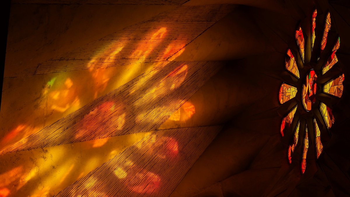 Afternoon sun floods the Sagrada Família through a fiery rose window, spilling pools of orange, scarlet, and emerald light across Gaudí's ribbed stone vault