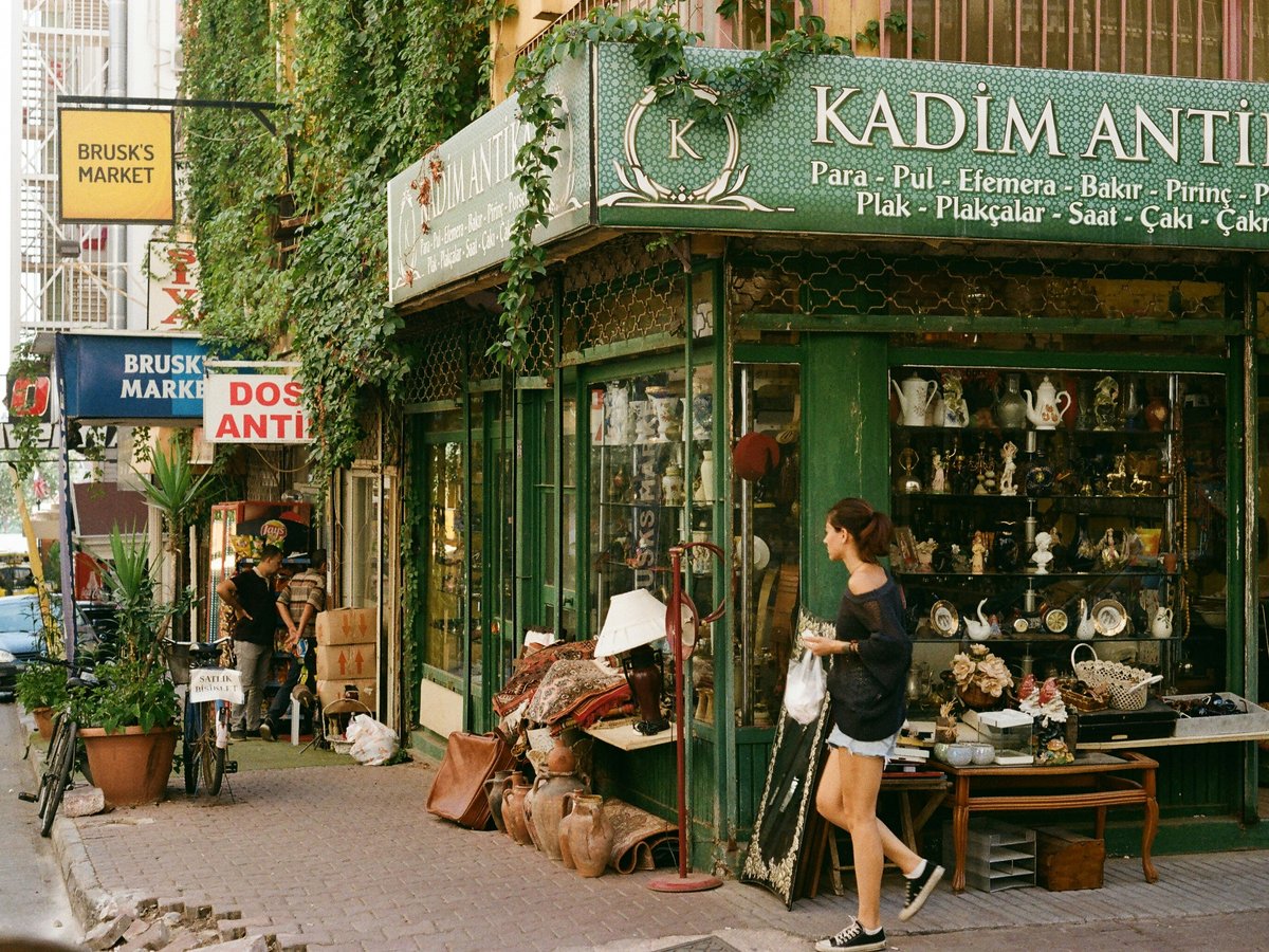 a woman is walking past a shop selling antiques