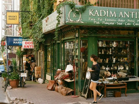 a woman is walking past a shop selling antiques