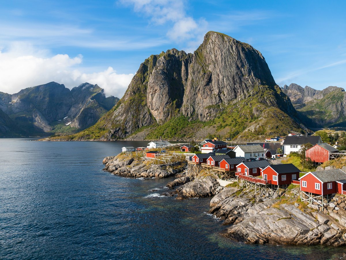 a group of houses by a body of water with mountains in the background with Lofoten in the background