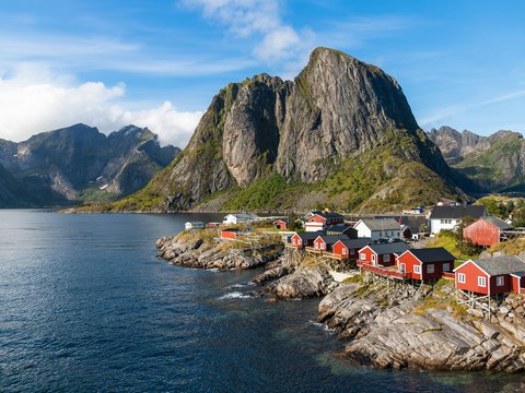 a group of houses by a body of water with mountains in the background with Lofoten in the background