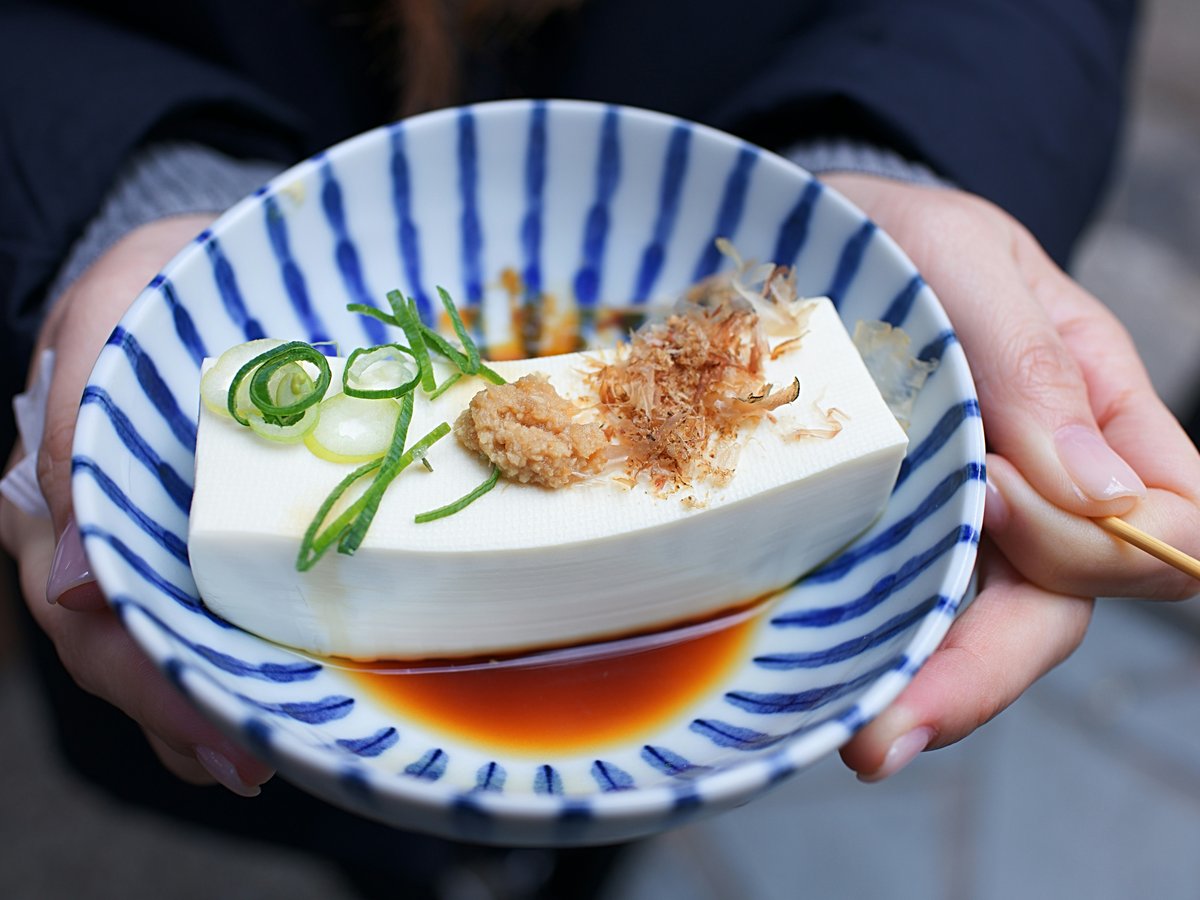 person holding white and blue ceramic plate with rice and sliced cucumber
