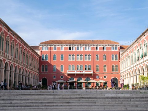 Grand pink building with arched colonnades and outdoor seating