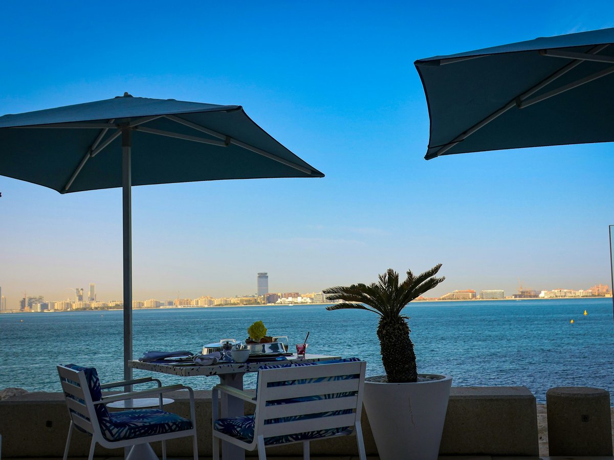 Restaurant tables overlook the ocean with umbrellas.