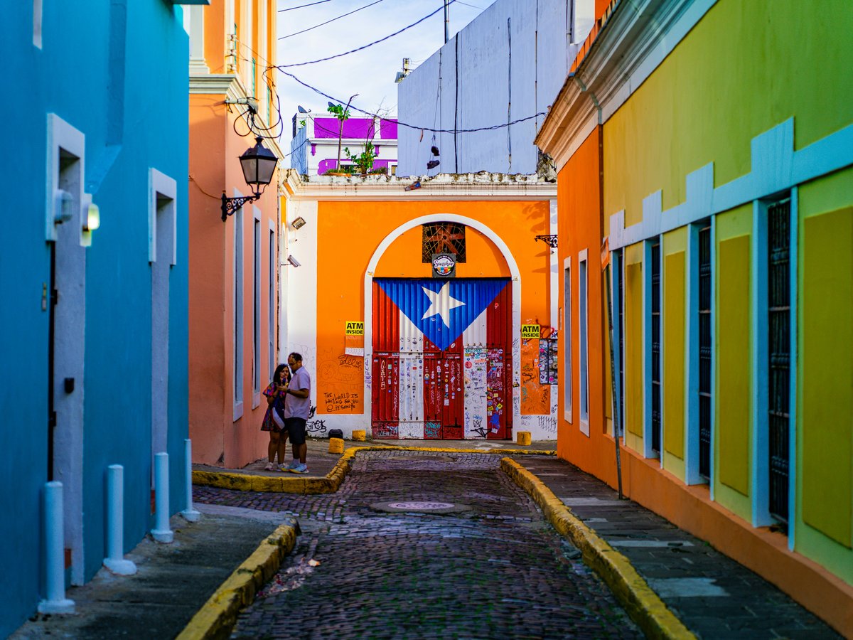 a narrow alley way with a colorful building and a flag on the door