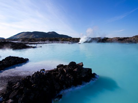 calm water beside mountain under white clouds and blue sky