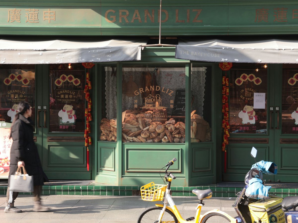 A woman walks past a green bakery storefront.
