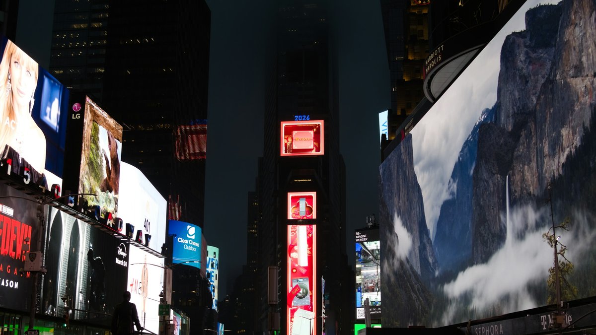 Times Square at night looking up the canyon of skyscrapers, every façade washed in the cool teal glow of Yosemite-cliff and Broadway billboards while a red 2026 advert stack anchors One Times Square at center
