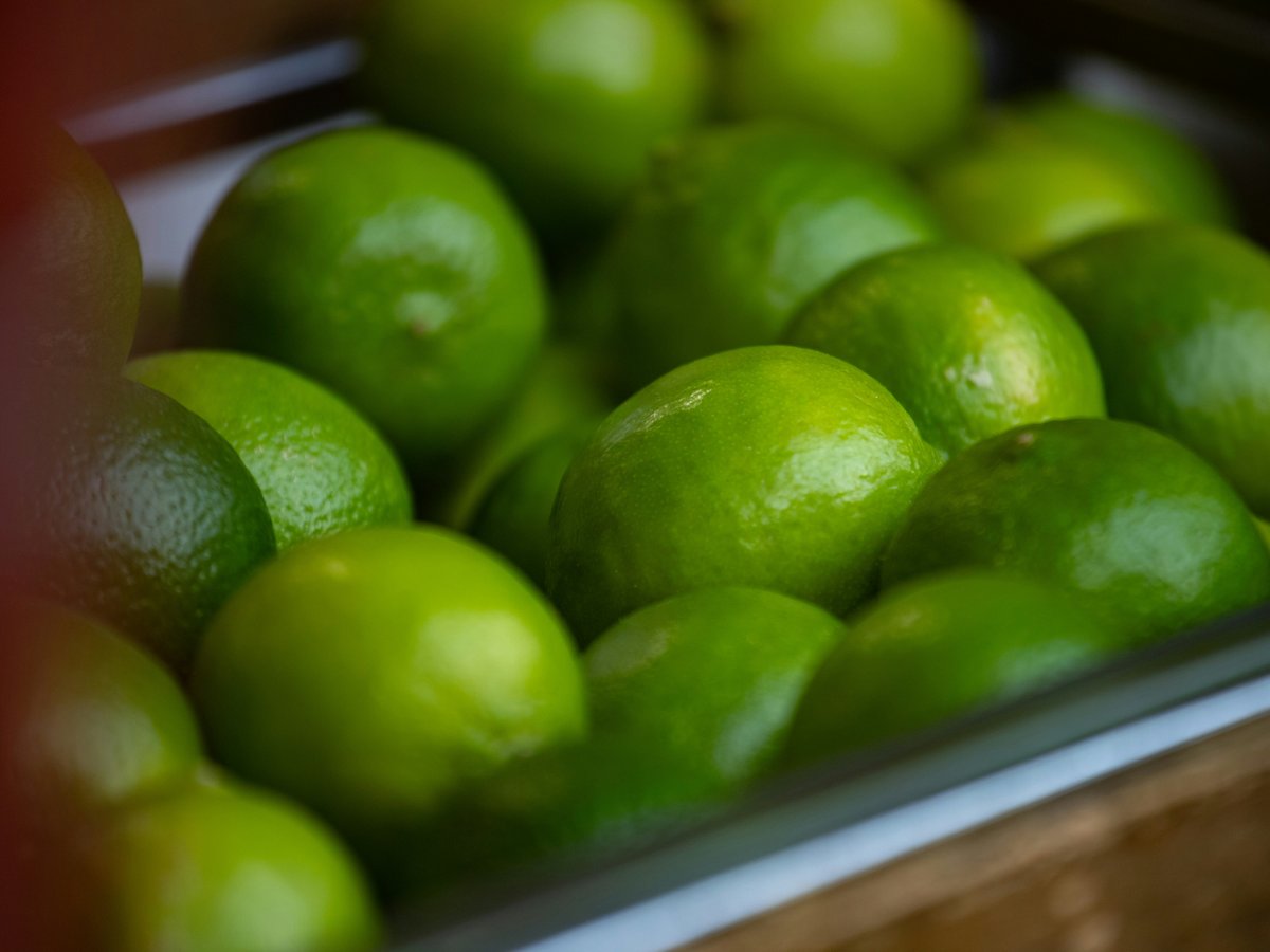 A close-up of many fresh green limes in a container.