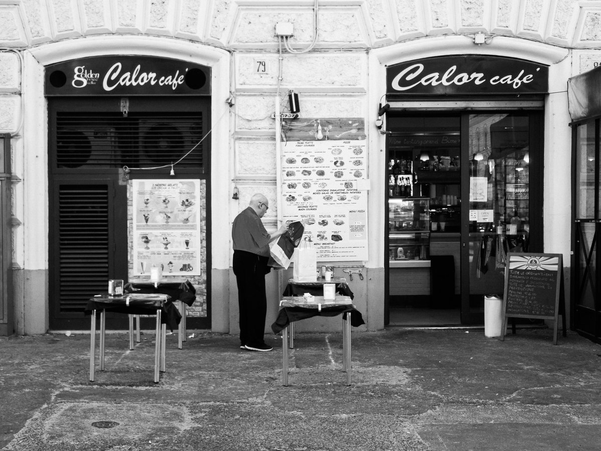 grayscale photo of man in black t-shirt and black pants standing near store