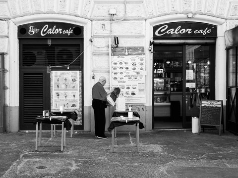grayscale photo of man in black t-shirt and black pants standing near store