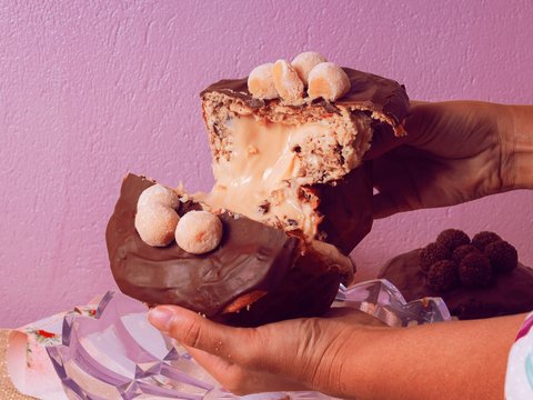 a person holding a piece of chocolate covered doughnut